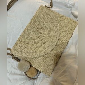 Straw crossbody purse with pom pom charms dangling from the side.